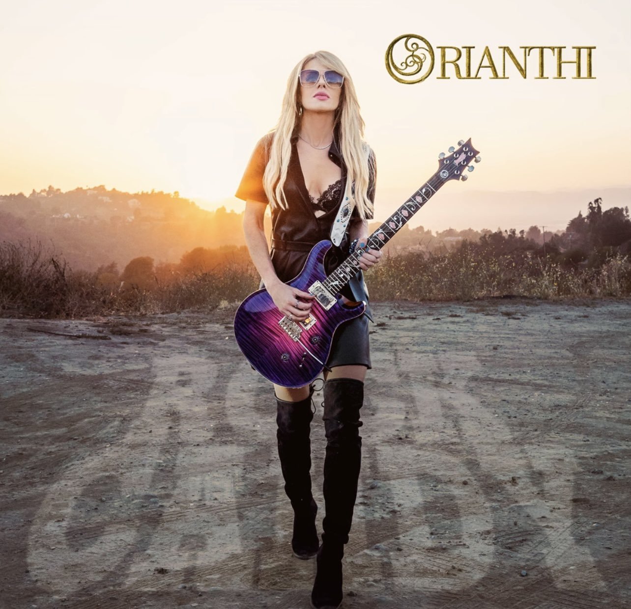 Cover of Orianthi's "Rock Candy" album; a woman walks toward the camera holding an electric guitar at sunset.